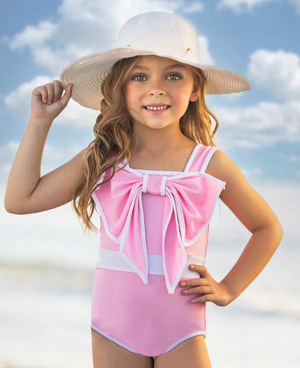 a girl wearing a pink Mia Belle swimsuit and a white hat